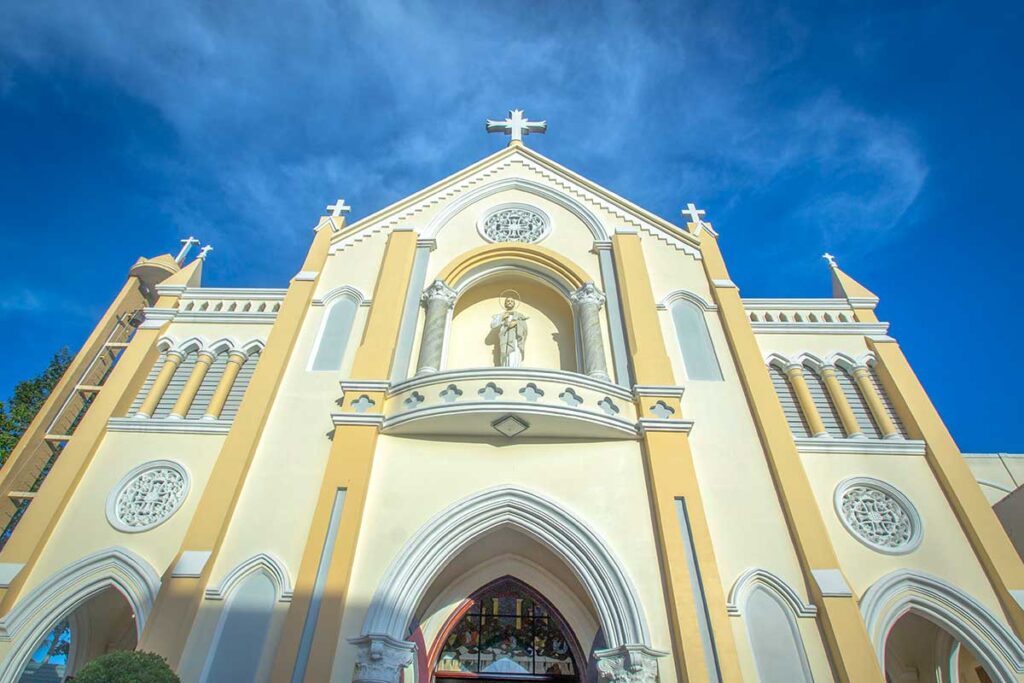 Close-up of My Tho Cathedral façade with statue niche, arched doorway, and round decorative windows in Tien Giang.