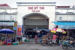 Busy gate of My Tho Central Market with street stalls and scooters in front