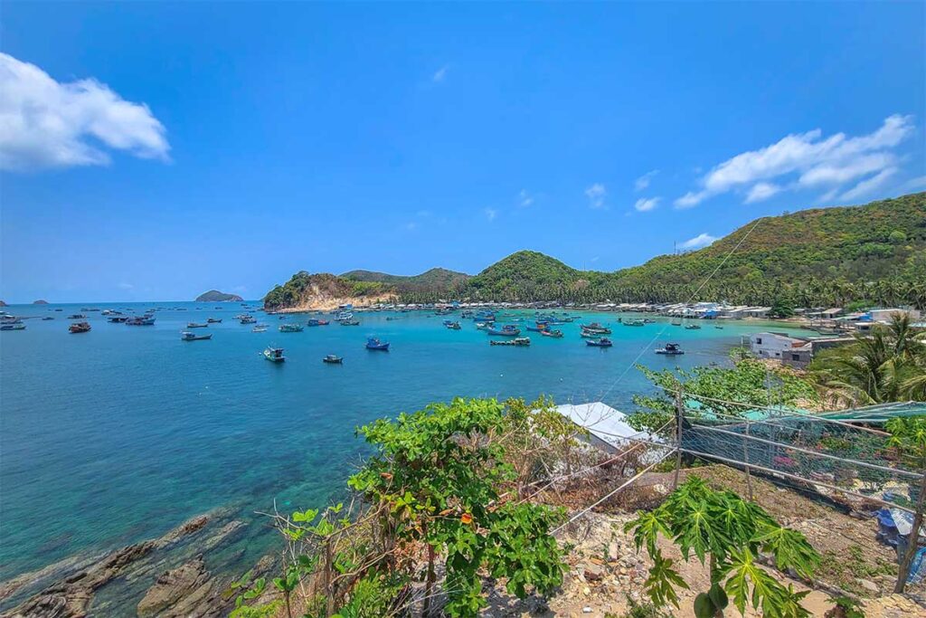 West coast view of Nam Du Island – Fishing boats anchored in calm turquoise water, with green hills and village coastline in the background.