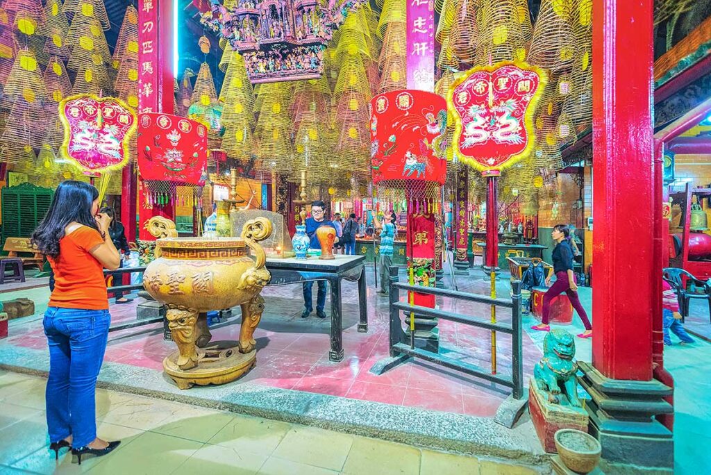 Interior of Ong Pagoda in Can Tho decorated with red lanterns, incense coils, and worshippers