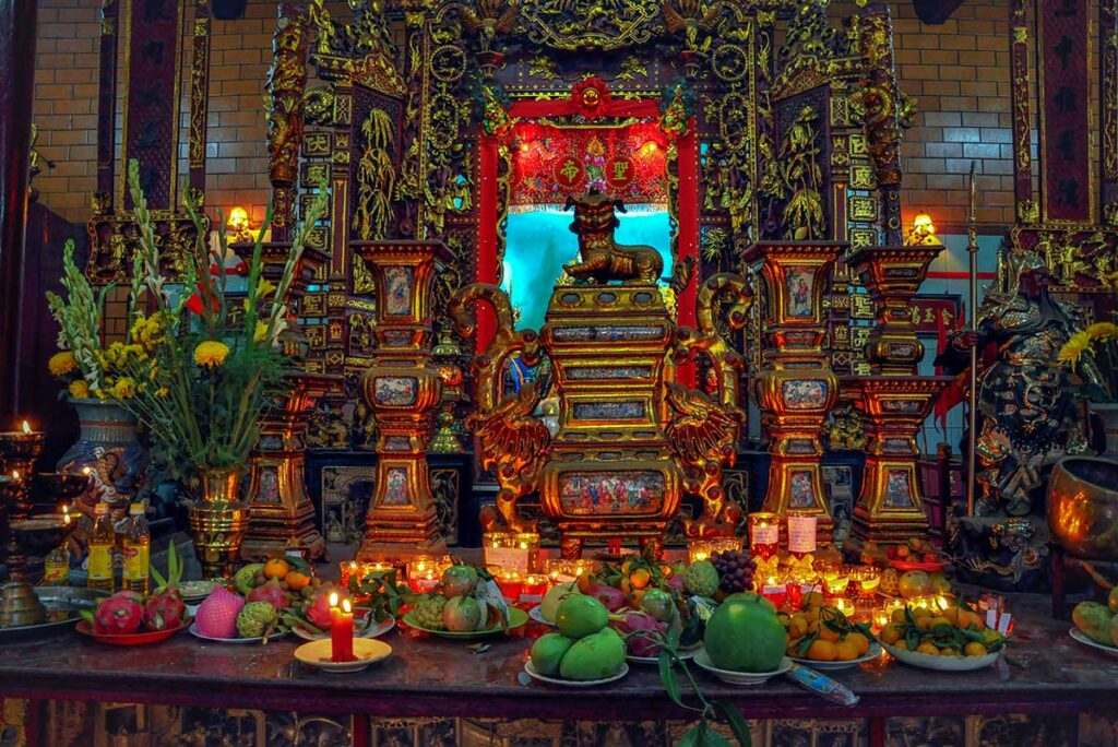 Ornate main altar of Ong Pagoda in Can Tho with gold carvings, candles, and fruit offerings
