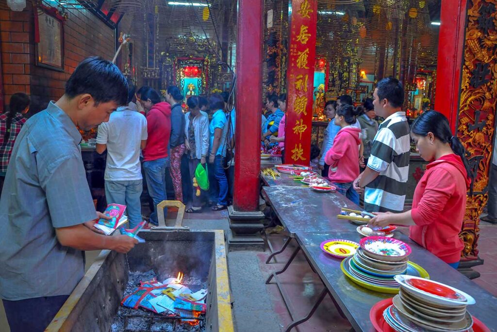 Inside Ong Pagoda during a ceremony with worshippers offering food and burning paper money in Can Tho