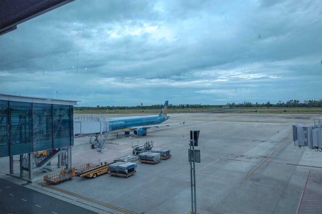 View through the glass looking outside Phu Bai International Airport with the landing strip and a plane of Vietnam Airlines 