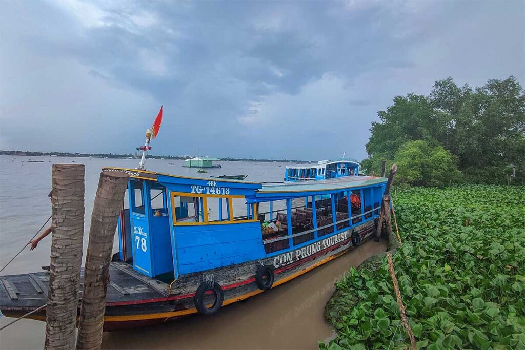 : Blue wooden boat marked “Con Phung Tourist” docked on the Tiền River at Phoenix Island, Ben Tre.