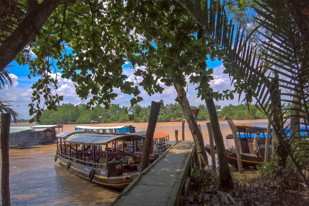 Tour boats docked at a pier on Phoenix Island, Ben Tre, surrounded by mangroves and river views.