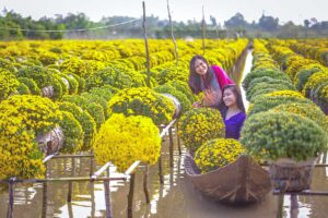 Woman in traditional áo dài paddling a sampan through flooded flower gardens in Sa Dec, Dong Thap