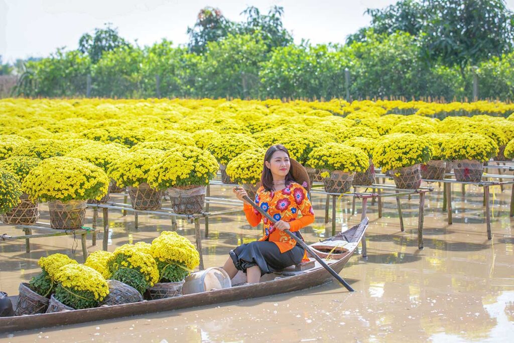 Tourist posing with yellow chrysanthemums while sitting in a wooden boat at Sa Dec Flower Village