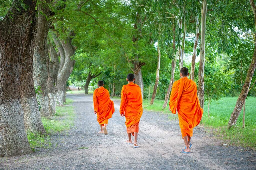 Buddhist monks walking along a tree-lined rural path near Sam Mountain, Chau Doc, An Giang.