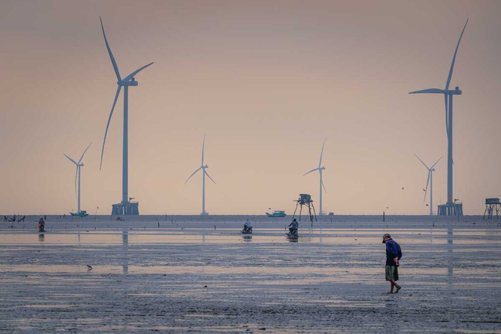 Wind farm and stilt fishing huts along the muddy coast of Tan Thanh Beach Tien Giang, Mekong Delta.