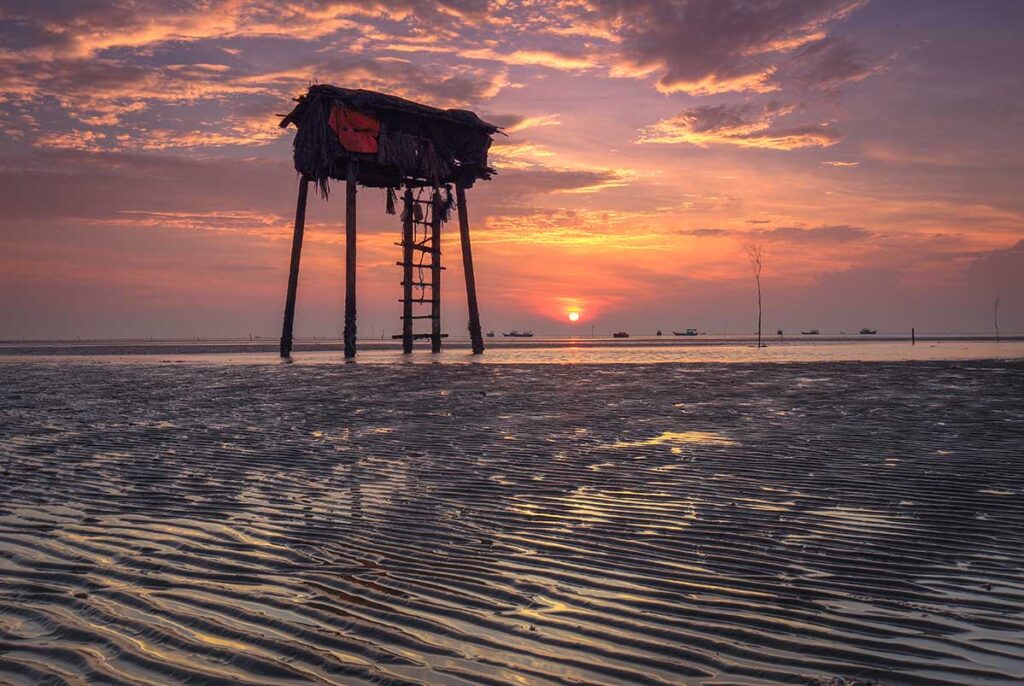 Stilted fishing hut at Tan Thanh Beach Tien Giang during a colorful sunset over the Mekong Delta coast.