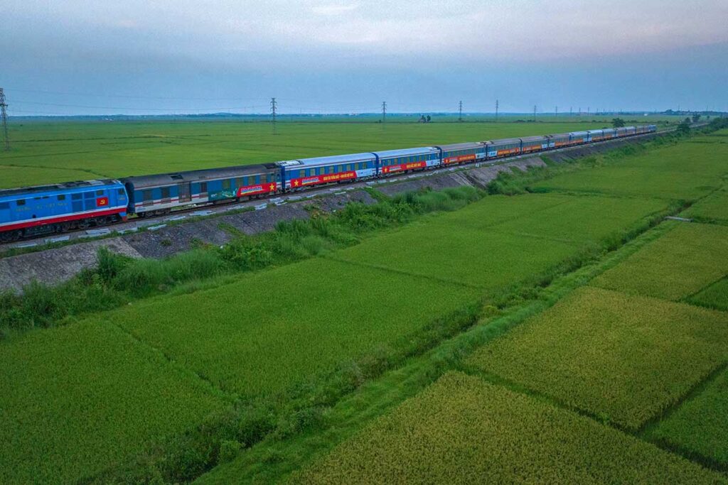 The Reunification Express Train of Vietnam rides through the countryside of Quang Binh with green rice fields on either side