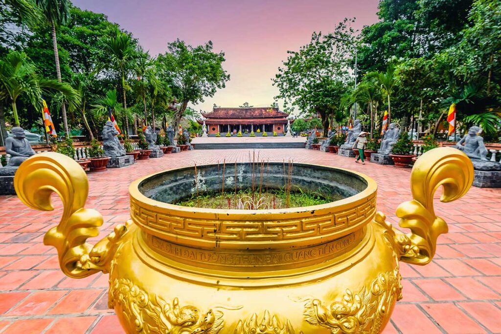 Golden incense urn in the courtyard of Truc Lam Phuong Nam Zen Monastery in Can Tho with the main hall in the background.