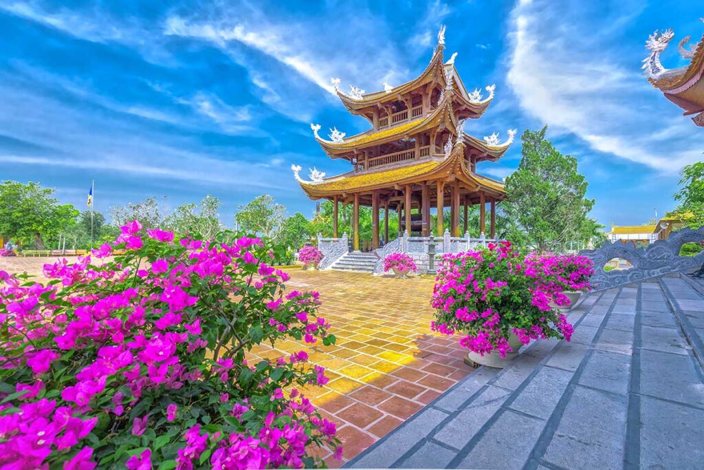 Wooden tower at Truc Lam Phuong Nam Zen Monastery in Can Tho with bougainvillea flowers in full bloom under a bright blue sky.
