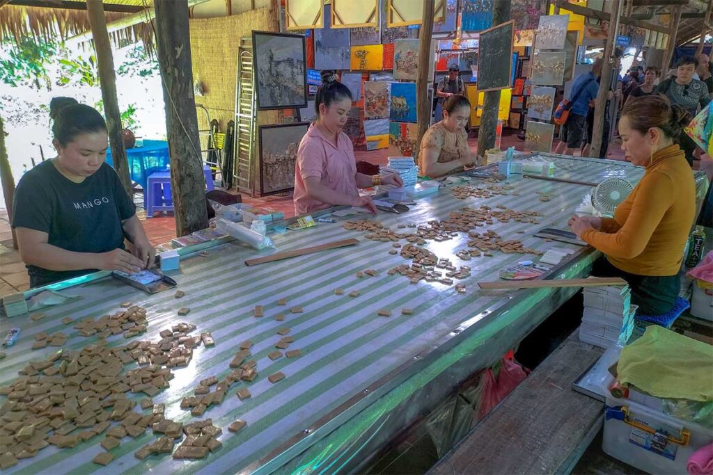Women wrapping freshly made coconut candy at a workshop on Unicorn Island, a common stop on Mekong Delta tours.