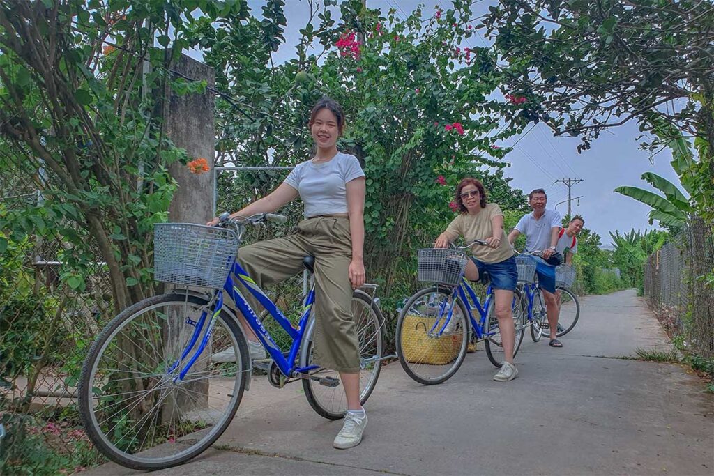 Family cycling tour on Unicorn Island (Thoi Son), passing village houses and orchards in the Mekong Delta countryside.