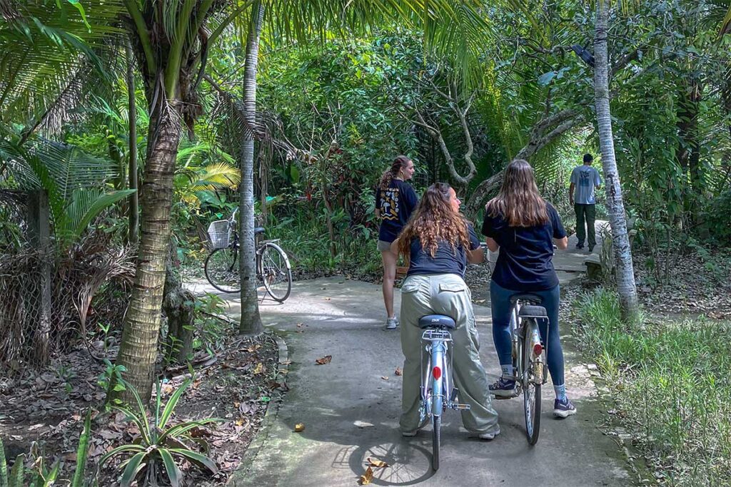 Travelers cycling along shaded concrete paths surrounded by tropical greenery on Unicorn Island (Thoi Son) in the Mekong Delta.