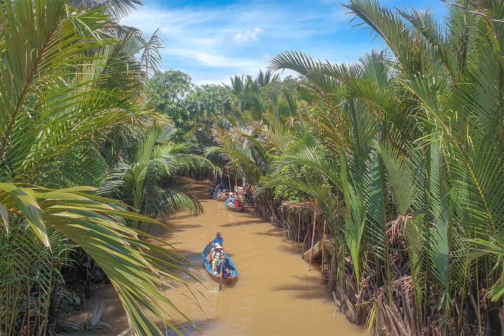 Narrow waterway lined with palm trees where tourists ride sampans on Unicorn Island in the Mekong Delta.