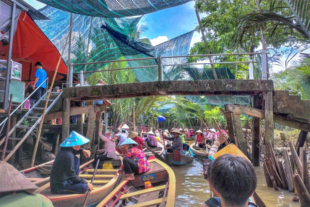 Tourists boarding sampan boats under shade nets for a crowded canal ride on Unicorn Island in the Mekong Delta.