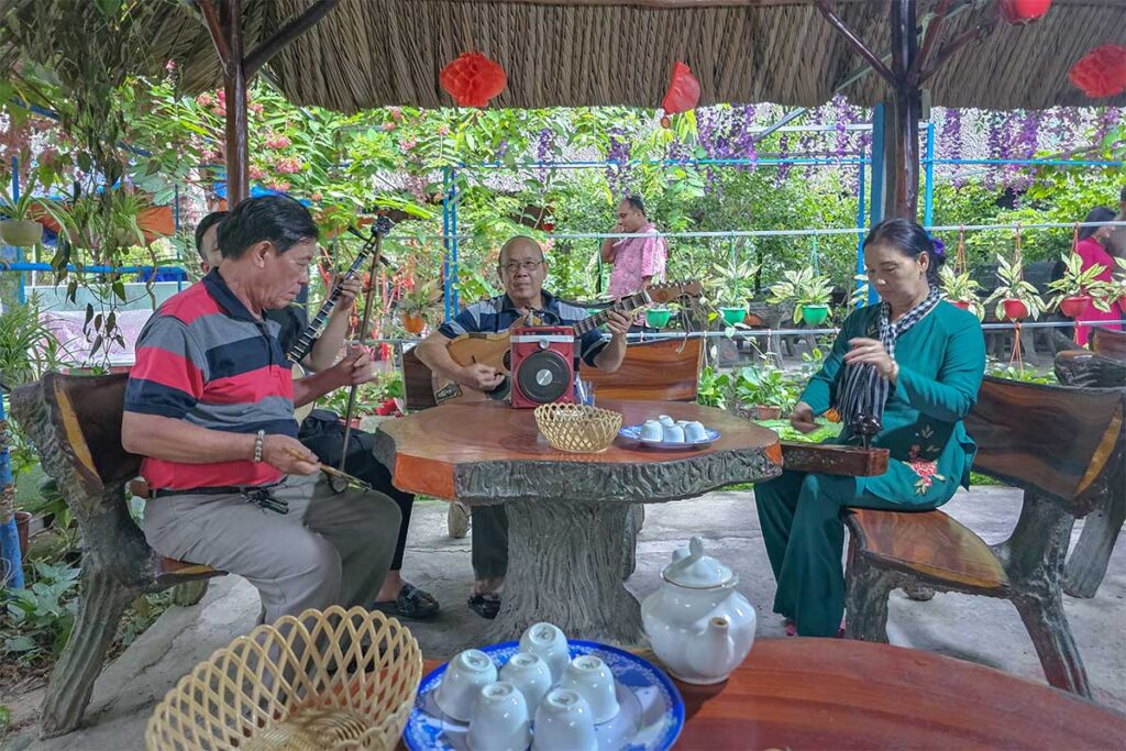 Group of local musicians performing Đờn Ca Tài Tử folk music with tea and fruit for visitors on Unicorn Island.