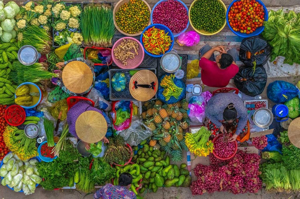 Aerial close-up of Vi Thanh Cho Hom market stalls showing colorful vegetables, herbs, and fruits laid out in baskets