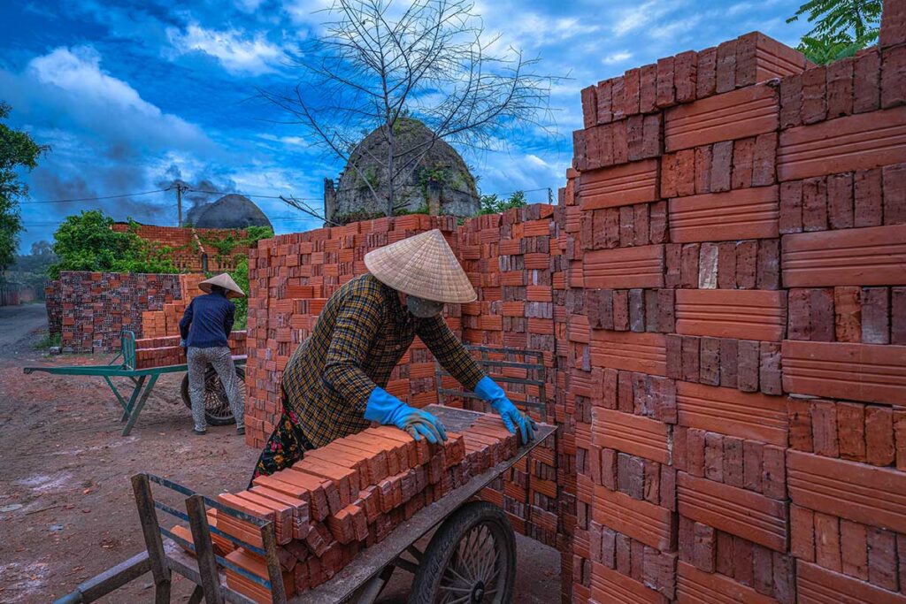 Local workers stacking red bricks by hand in Mang Thit pottery village