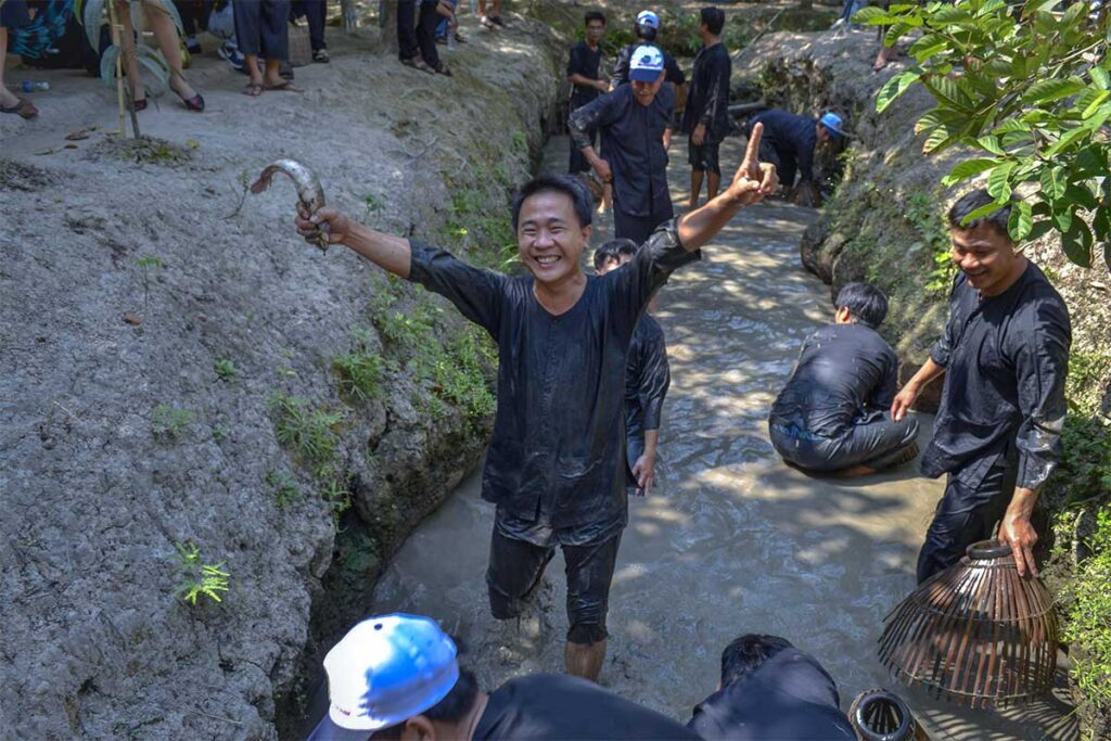 A Vietnamese tourist is happy with catching a fish in a mud pool at Vinh Sang Tourist Area
