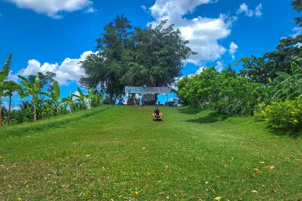 A traveller is sliding down a grass hill at Vinh Sang Tourist Area