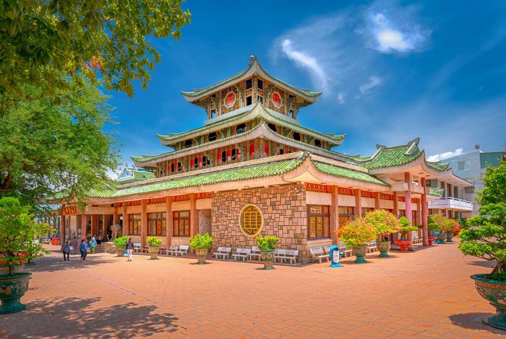 Side view of Ba Chua Xu Temple in Chau Doc, showing the lotus-shaped rooflines, tiled courtyard, and potted plants.