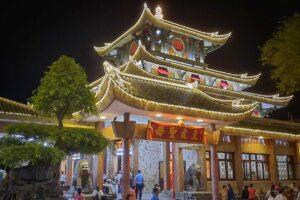 Ba Chua Xu Temple illuminated at night in Chau Doc, with glowing rooflines and worshippers entering the main hall.