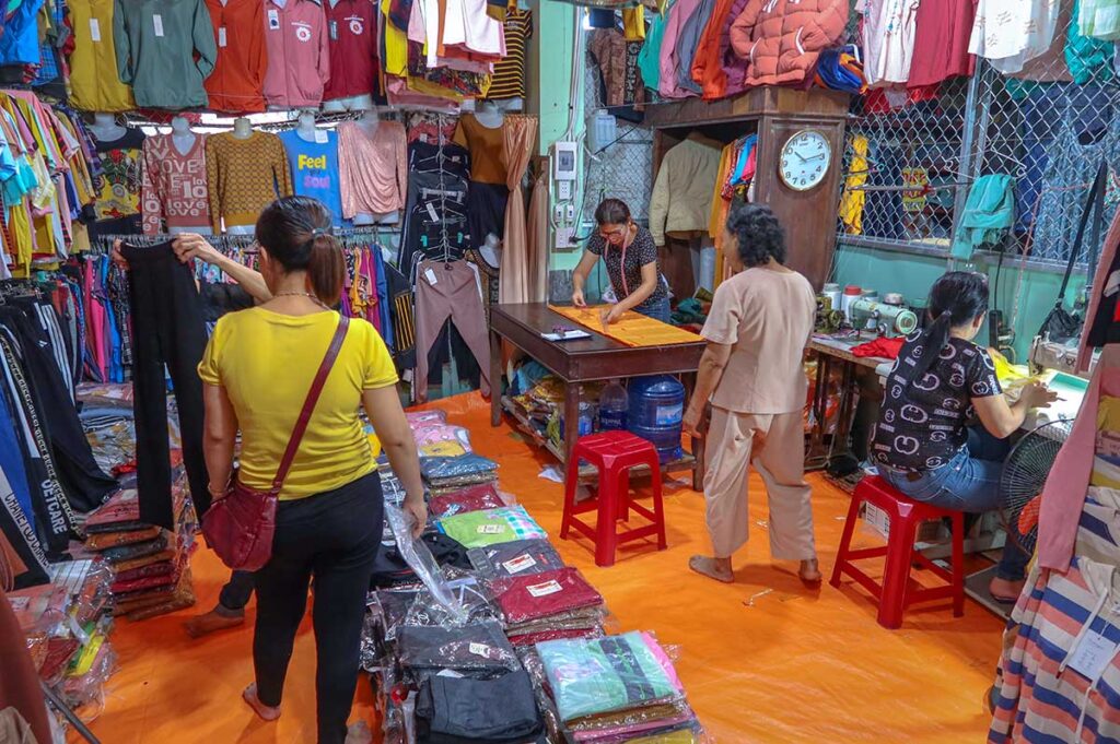 Busy clothing stall at Ba Le Market in Hoi An where vendors sell everyday wear and provide on-the-spot tailoring for local customers