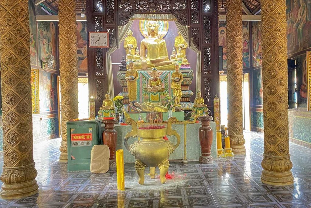 Interior of Bat Pagoda (Chùa Dơi) main hall in Soc Trang with golden Buddha statues, detailed murals, and carved wooden pillars.