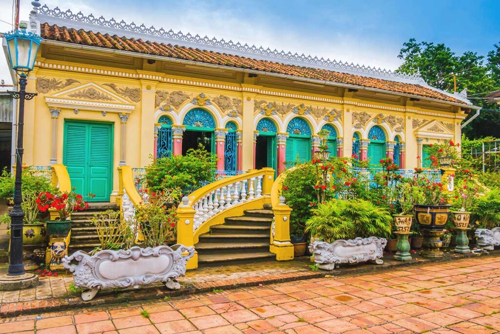 Front façade of Binh Thuy Ancient House with yellow French-style exterior, green shutters, and ornate staircases in Can Tho.