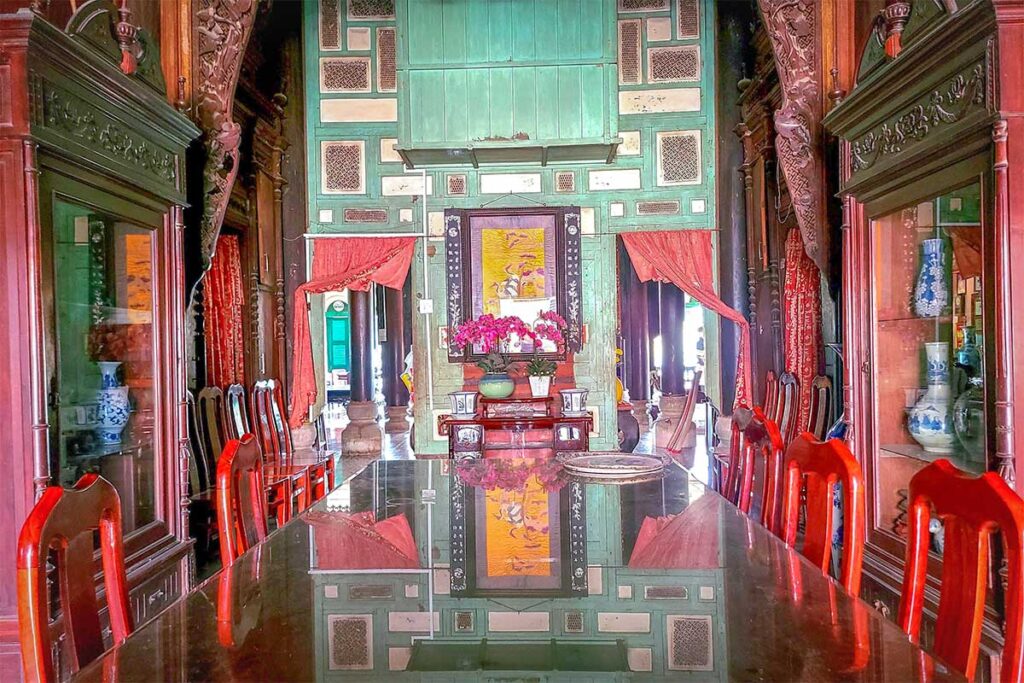 Interior of Binh Thuy Ancient House showing ancestor altar, carved wooden furniture, and long dining table.