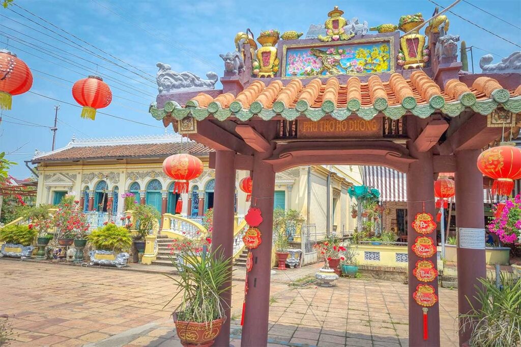 Entrance gate with red lanterns and decorative roof opening to Binh Thuy Ancient House courtyard in Can Tho.