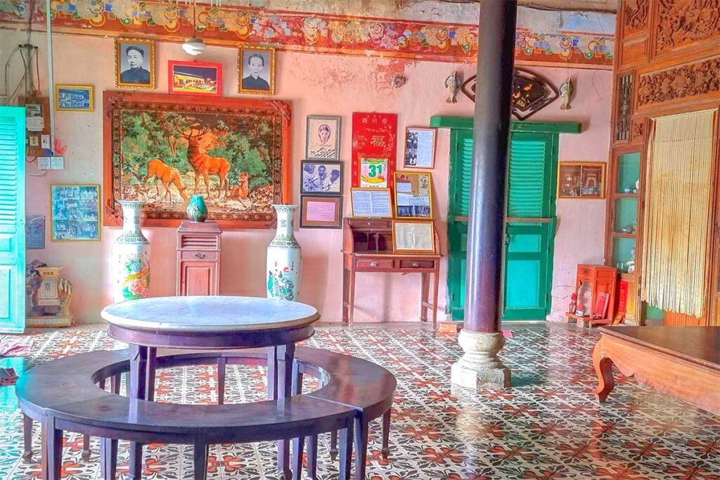 Marble table and wooden round chairs in a traditional interior room of Binh Thuy Ancient House, decorated with portraits and vases.