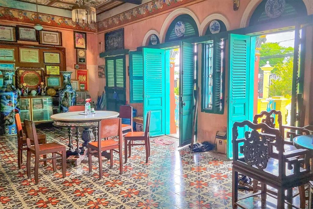 Sitting area with mosaic tile floor, antique chairs, and turquoise shutters inside Binh Thuy Ancient House.
