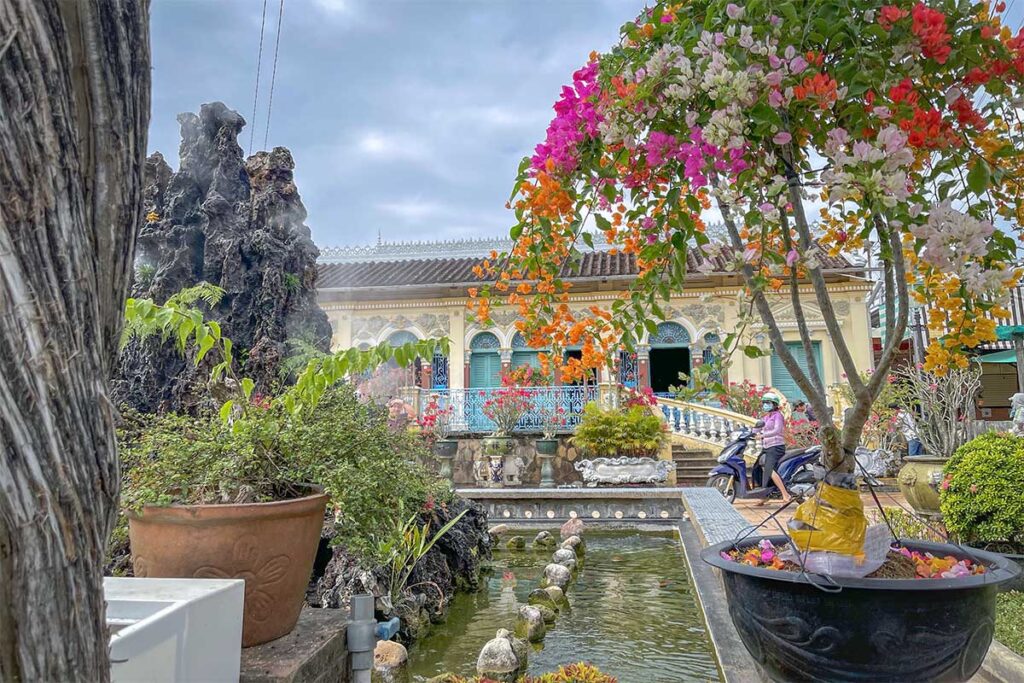 Garden pond and bonsai trees in front of Binh Thuy Ancient House with bougainvillea in bloom.
