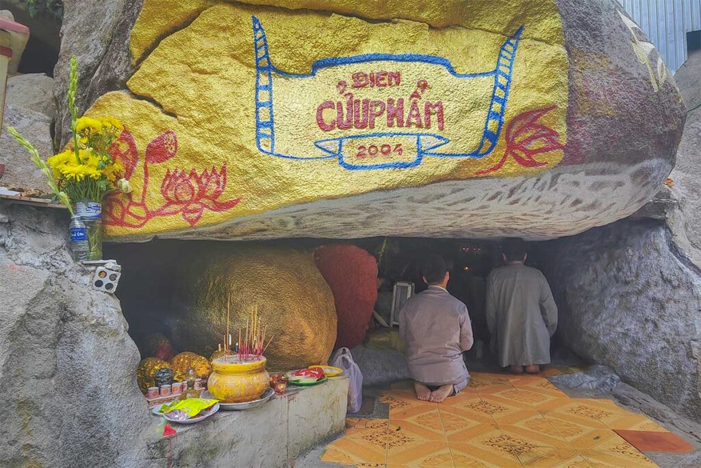 Cave shrine on Cam Mountain – Worshippers praying inside a small cave temple with golden rock inscriptions on Forbidden Mountain, An Giang.