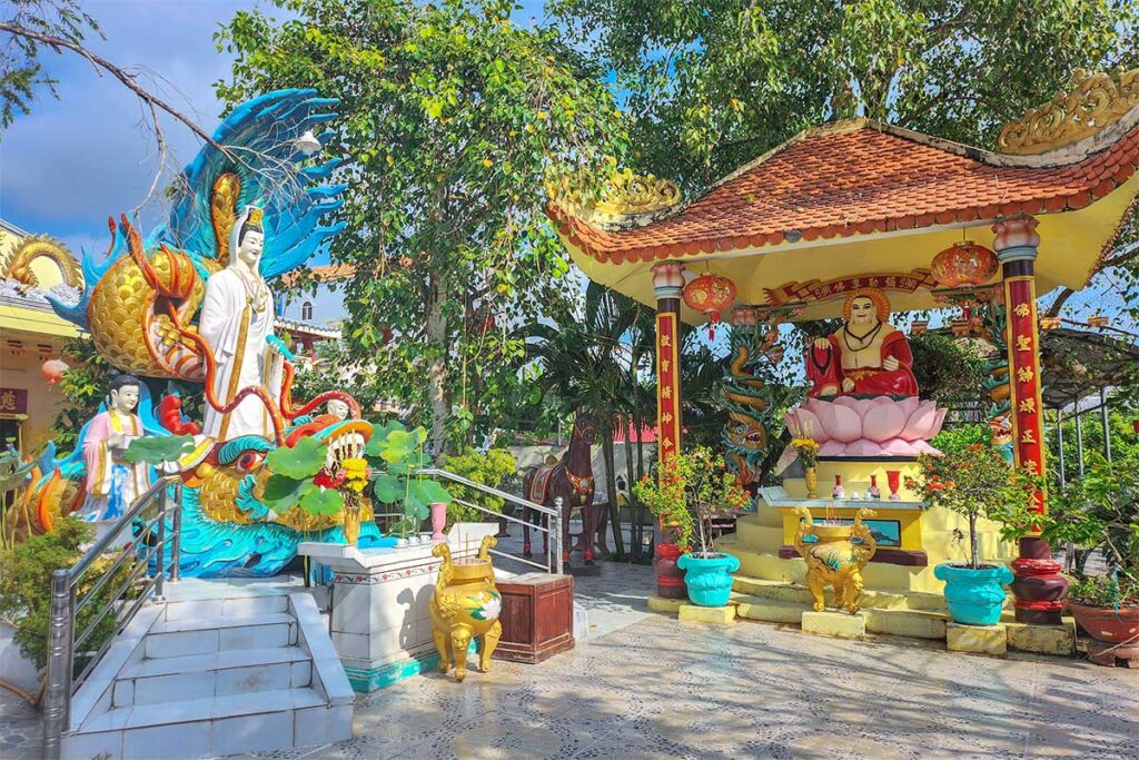 Clay Pagoda courtyard with Guanyin and Maitreya statues – Outdoor statues of Guanyin and the Laughing Buddha on lotus pedestals in the colorful courtyard of Chùa Đất Sét.