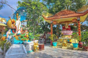 Clay Pagoda courtyard with Guanyin and Maitreya statues – Outdoor statues of Guanyin and the Laughing Buddha on lotus pedestals in the colorful courtyard of Chùa Đất Sét.
