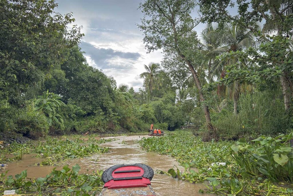 Rowing a small boat through narrow canals lined with coconut trees on Con Son Islet, Mekong Delta