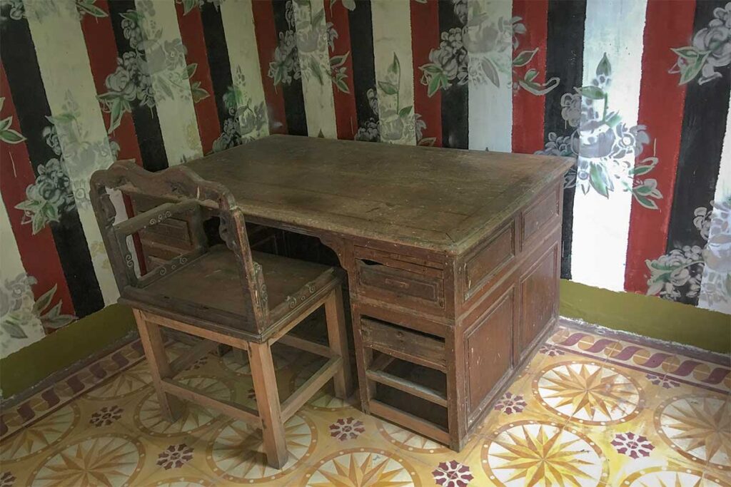 Old wooden desk and chair in a side room of Huynh Ky Ancient House, showing simple antique furniture.
