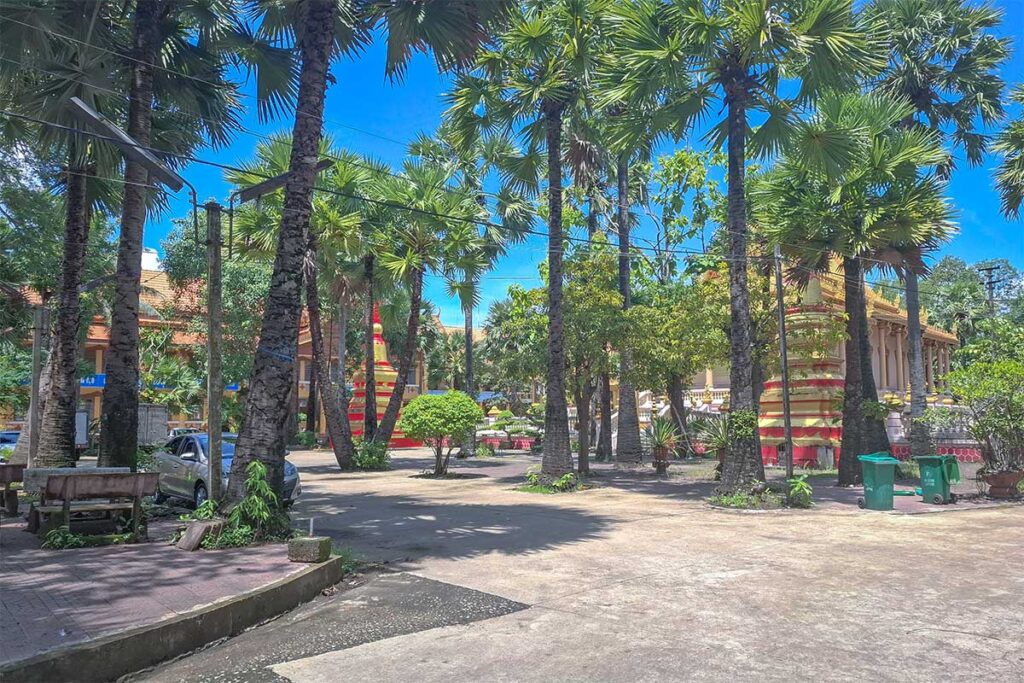 Shady palm-lined courtyard of Kh’leang Pagoda in Soc Trang, with stupas and temple buildings in view.