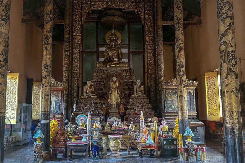 Interior of Kh’leang Pagoda in Soc Trang, with a large gilded Buddha statue surrounded by smaller images and golden lacquered columns.