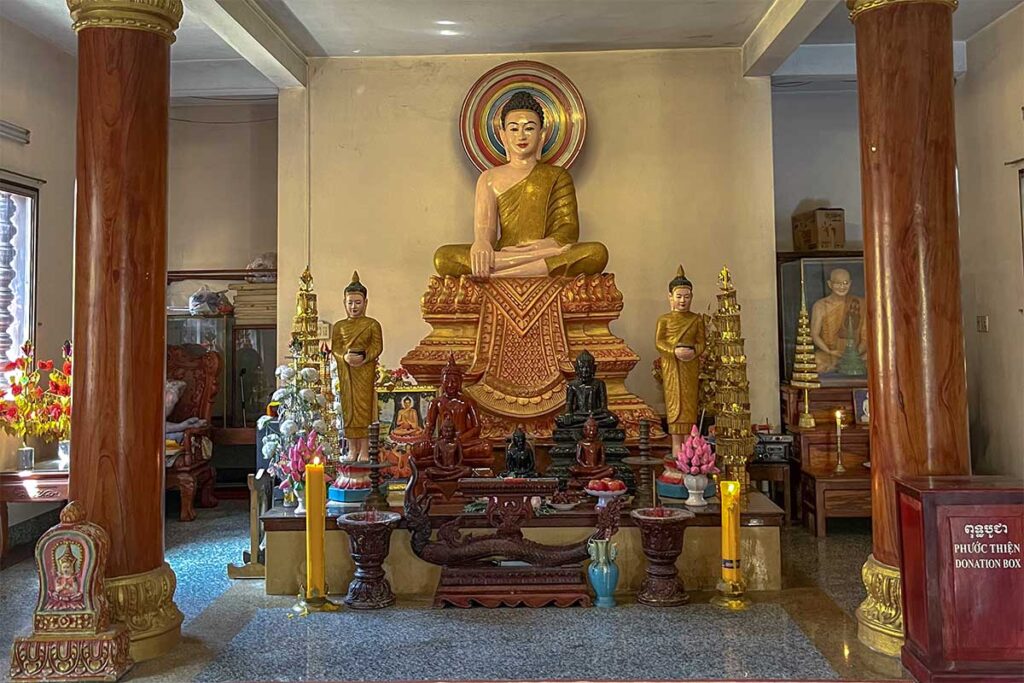 Main Buddha altar inside Muniransay Khmer Buddhist Temple in Can Tho with golden Shakyamuni statue and smaller Buddha images.