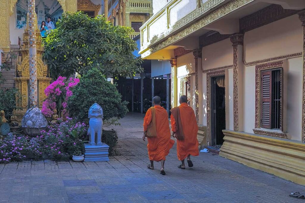Two monks in orange robes walking in the courtyard of Muniransay Khmer Buddhist Temple in Can Tho.
