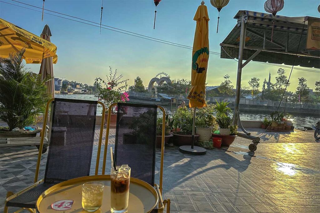 Canal-side café in Nga Nam town with iced coffee and evening view of the river.