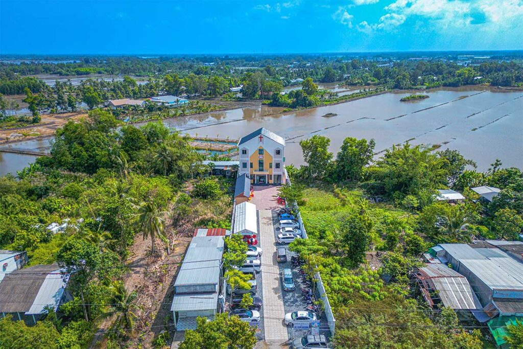 Countryside view of Nga Nam with rice fields, canals, and a small church surrounded by greenery.