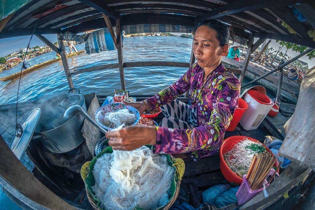 Local woman preparing noodle soup on a floating eatery boat at Nga Nam Floating Market, Soc Trang.