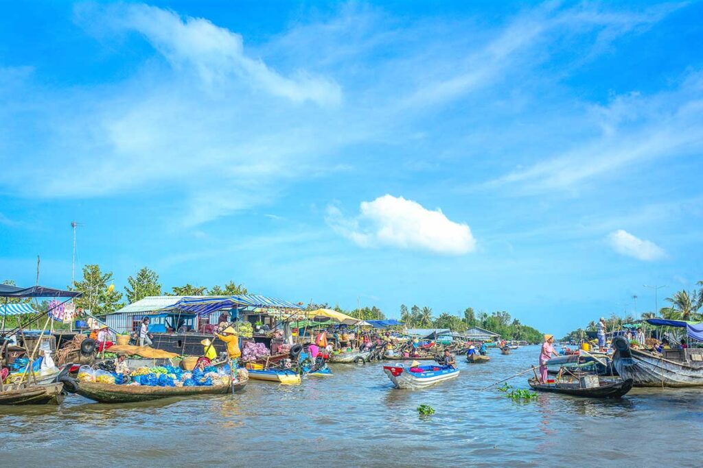 Wide view of Nga Nam Floating Market showing dozens of boats selling produce on the river under a bright blue sky.